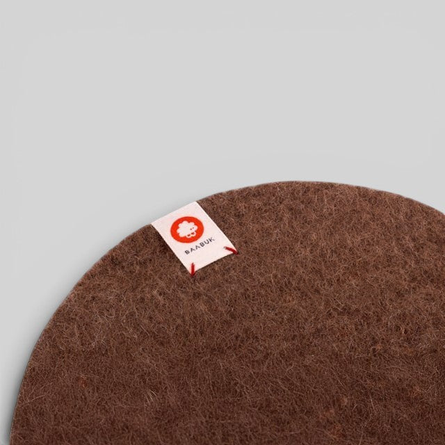 Baabuk brown felted wool trivet hot plate with a small branded fabric tag on a neutral background
