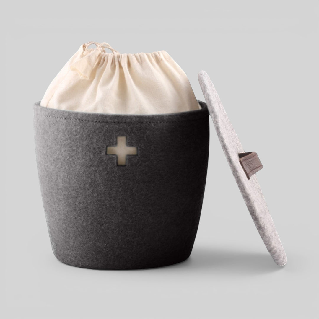 Baabuk dark grey felted wool basket with a Swiss cross cutout, leather strap lid, and internal fabric liner.