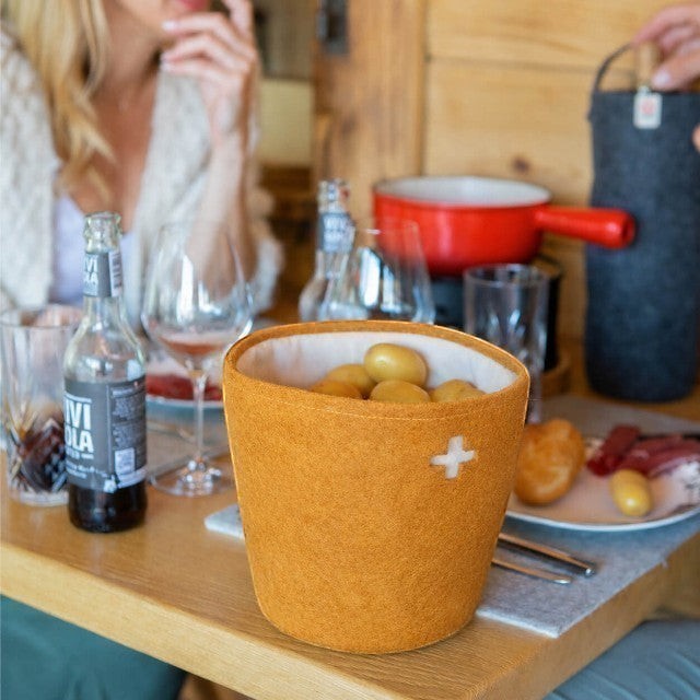 Baabuk honey-colored felted wool basket with a Swiss cross cutout, used as a potato server on a dining table.