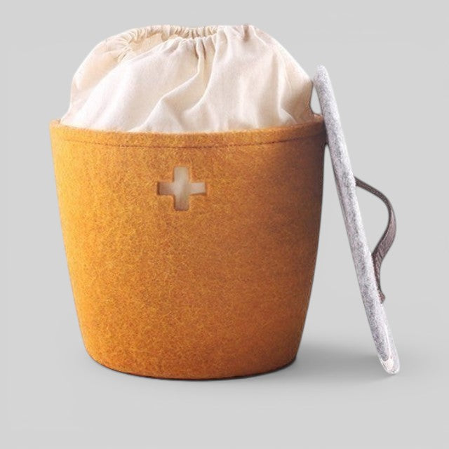 Baabuk honey yellow felted wool basket with a Swiss cross cutout, fabric liner, and a grey lid with leather handle.
