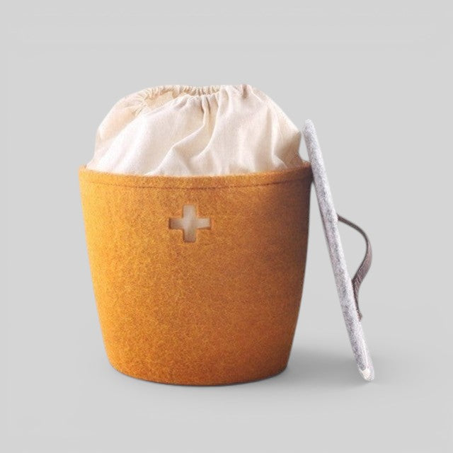 Baabuk honey yellow felted wool basket with Swiss cross cutout, fabric liner, and grey lid with leather handle.