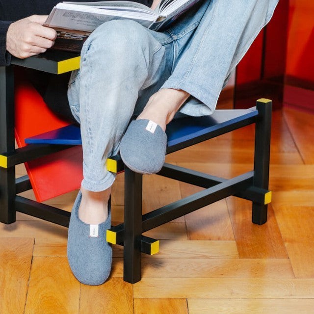 Baabuk Kanga grey wool slippers worn by a person sitting on a modern chair while reading a book