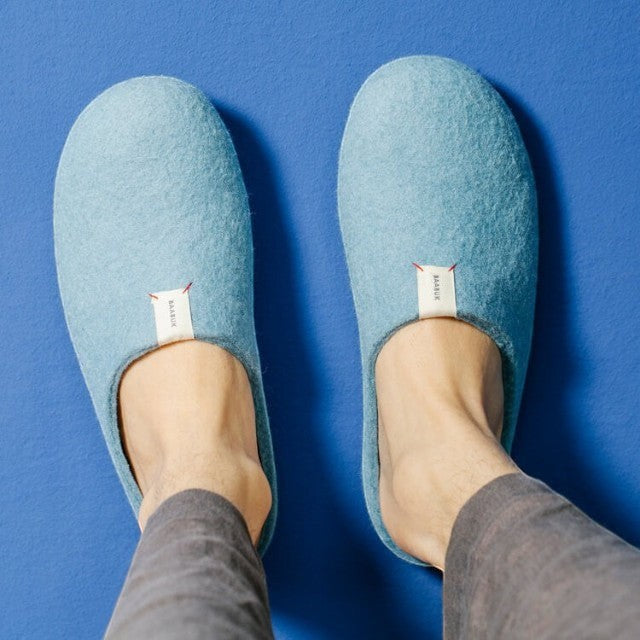 Baabuk Kanga light blue handmade wool slippers worn on feet against a blue background