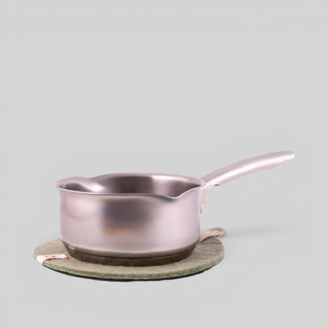 Baabuk khaki felted wool trivet hot plate with a leather strap under a metal saucepan on a light grey background
