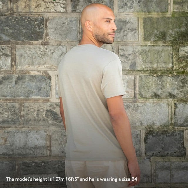 Baabuk khaki 100% merino wool T-shirt worn by a model standing against a stone wall.
