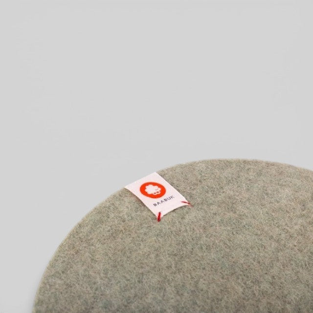 Baabuk khaki felted wool trivet hot plate with a small branded fabric tag on a neutral background