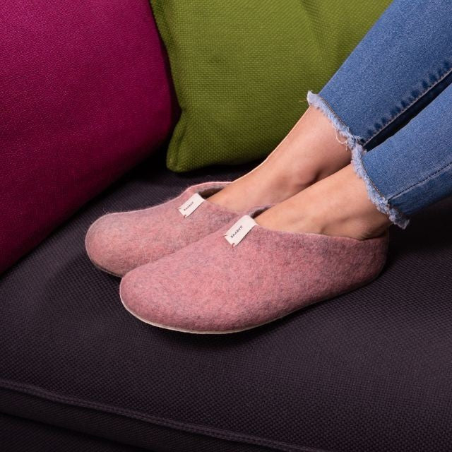 Baabuk Mel pink wool slippers with crepe rubber soles worn by a person on a dark sofa with green and pink cushions.