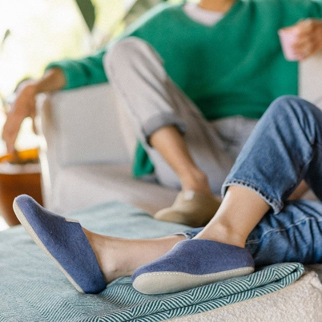 Baabuk Mel purple wool slippers worn by a person relaxing on a sofa with a green sweater and blue jeans