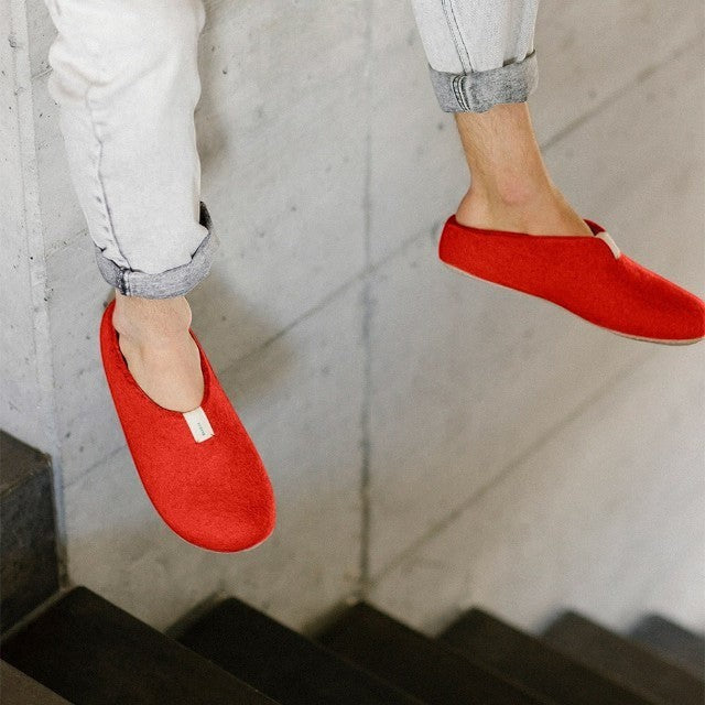 Baabuk Mel slippers in salsa red wool with natural crepe rubber soles worn on feet against a concrete background
