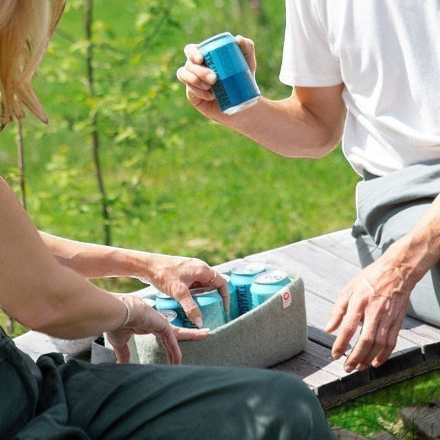Baabuk light blue wool beer cooler holding cans on a wooden bench outdoors. Natural wool, handmade.